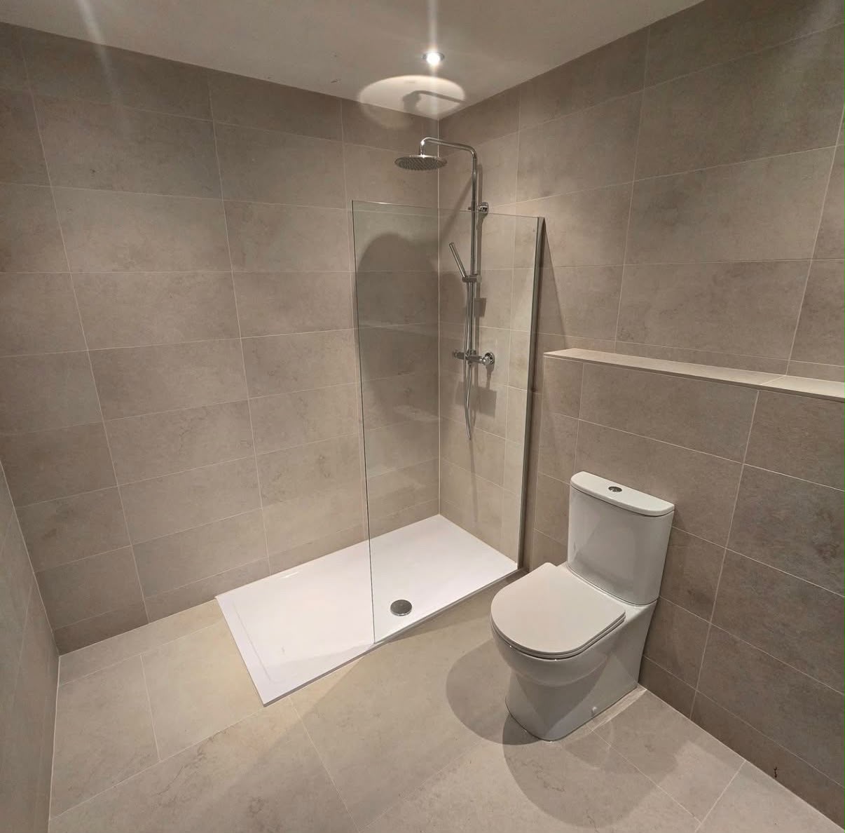 Neutral en-suite bathroom with stone-effect tiles, frameless shower panel and chrome rainfall shower