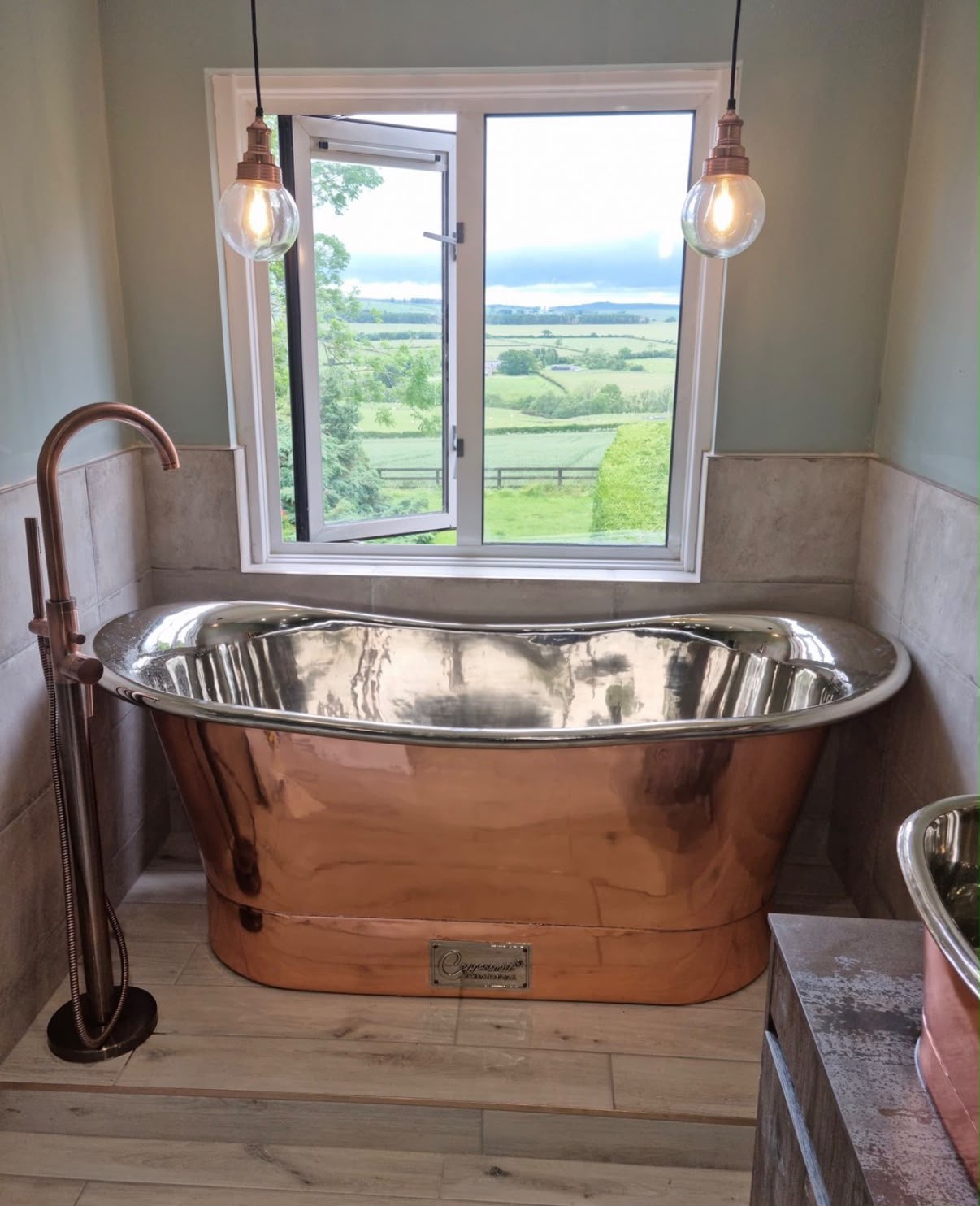 Country bathroom with a freestanding polished copper bathtub beneath an open window